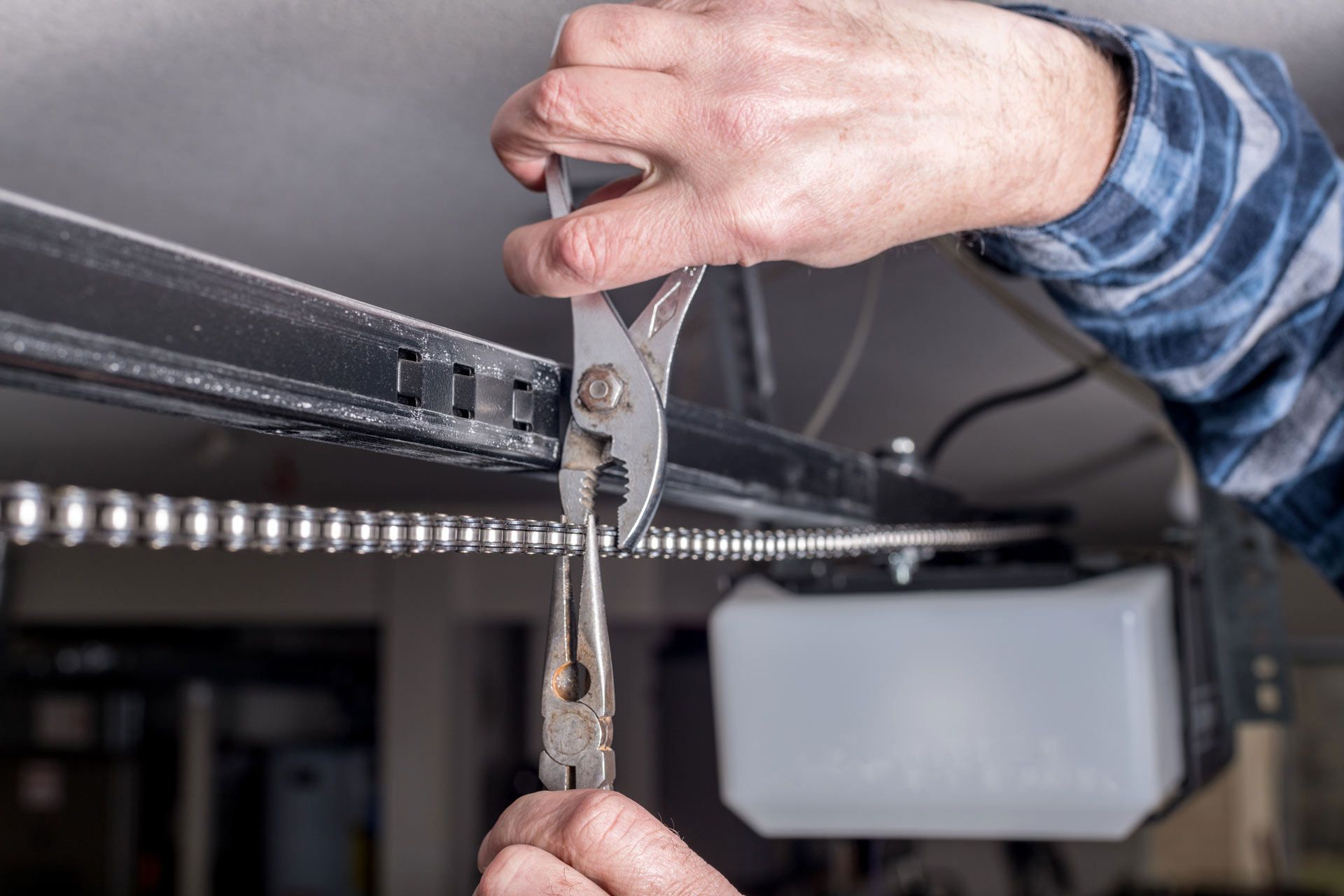 Professional technician performing garage door operator repair on a heavy-duty metal drive chain.