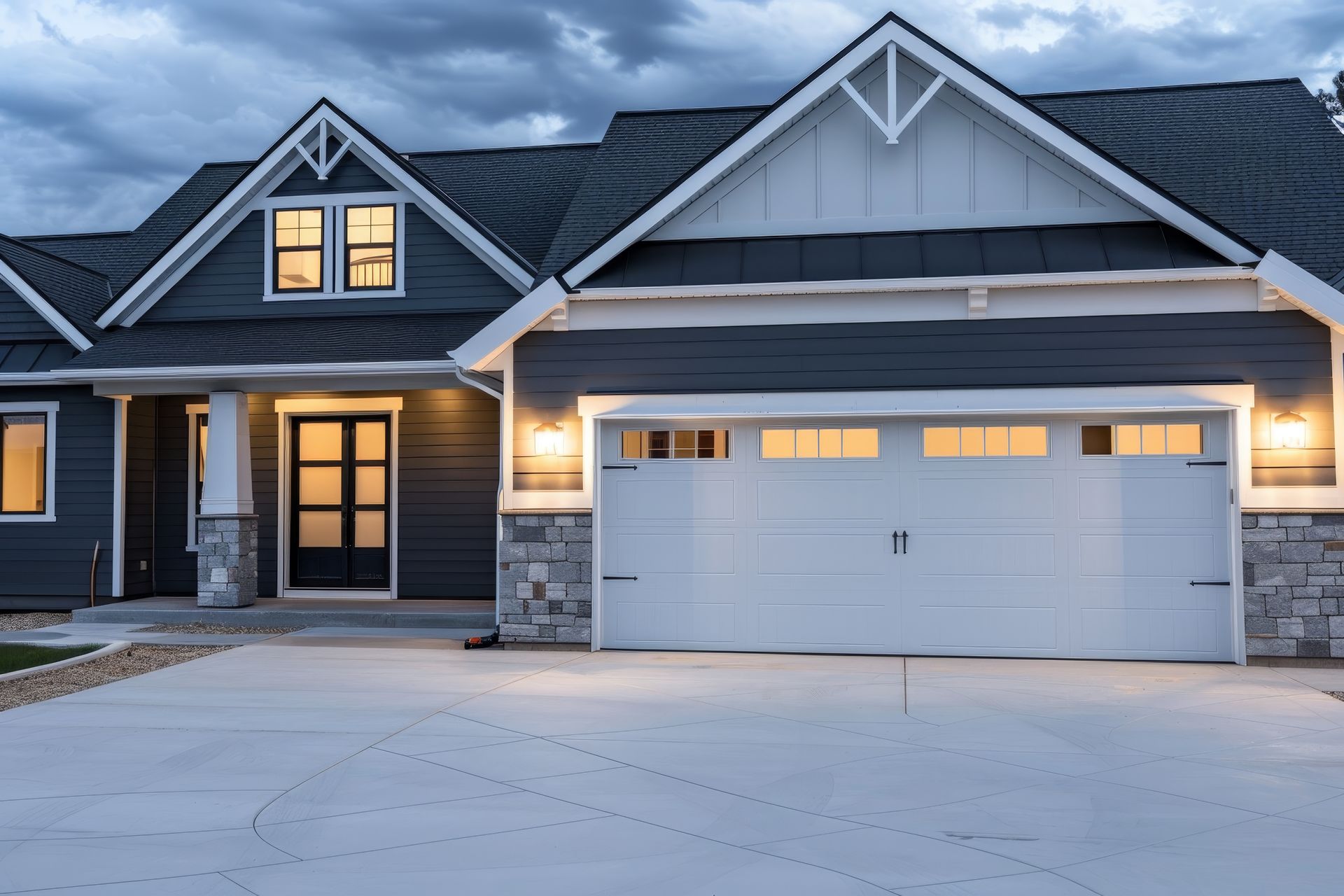 Modern house exterior with lit entryway and large white garage door at dusk.