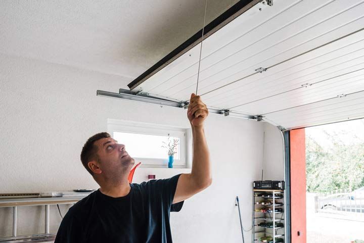 Person pulling cord to adjust sectional garage door system during repair or maintenance.