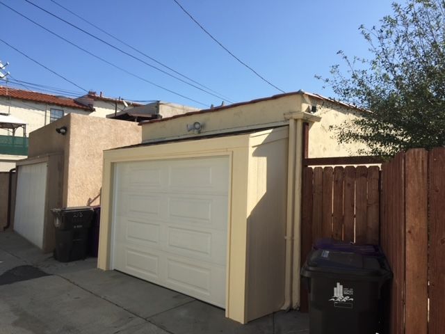 Garages in a narrow alleyway with a white garage door and a wooden fence. Sunny day.