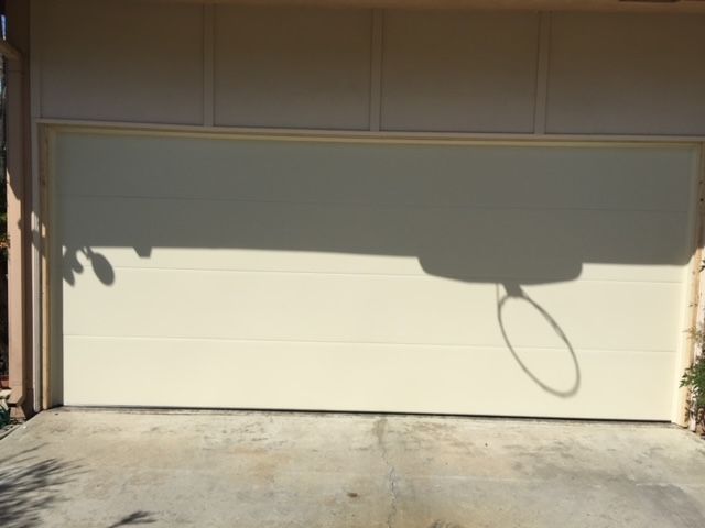 Beige garage door with a basketball hoop's shadow cast on it.