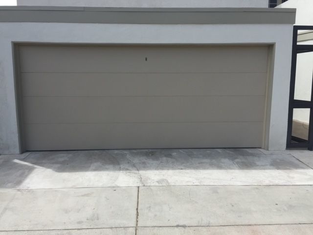Beige garage door set into a white frame with a concrete driveway in front.