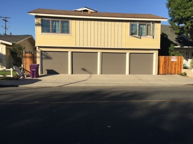 Two-story yellow house with three brown garage doors, two windows, and a brown roof.