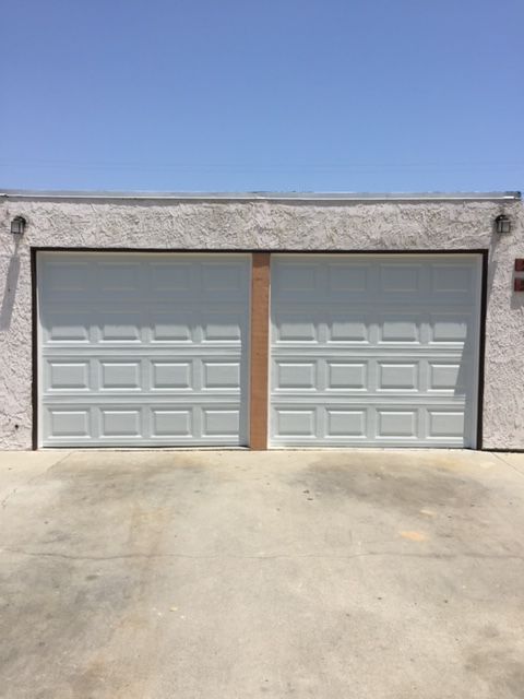 Two white garage doors with rectangular panels under a clear blue sky.