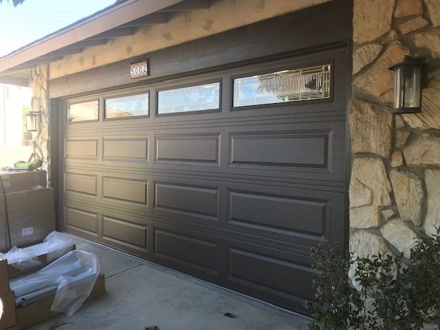 Brown garage door with windows, next to a stone wall and outdoor light.