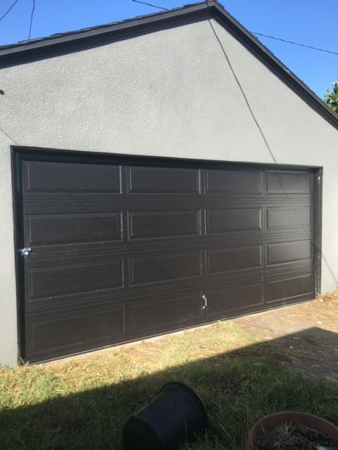 Black garage door on a gray stucco building with green grass in front.