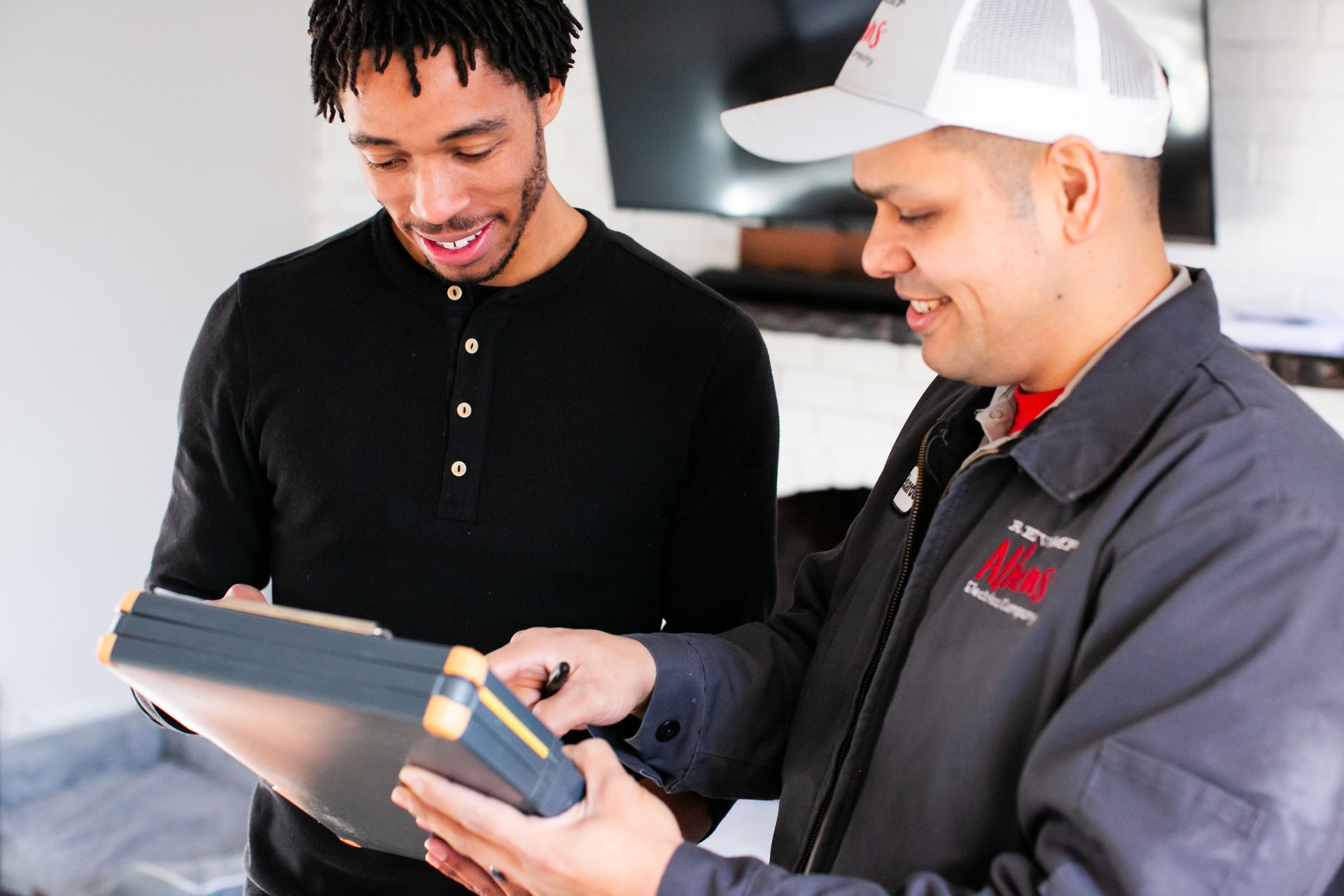 Two workers reviewing a tablet together in a workshop, one pointing at the screen.