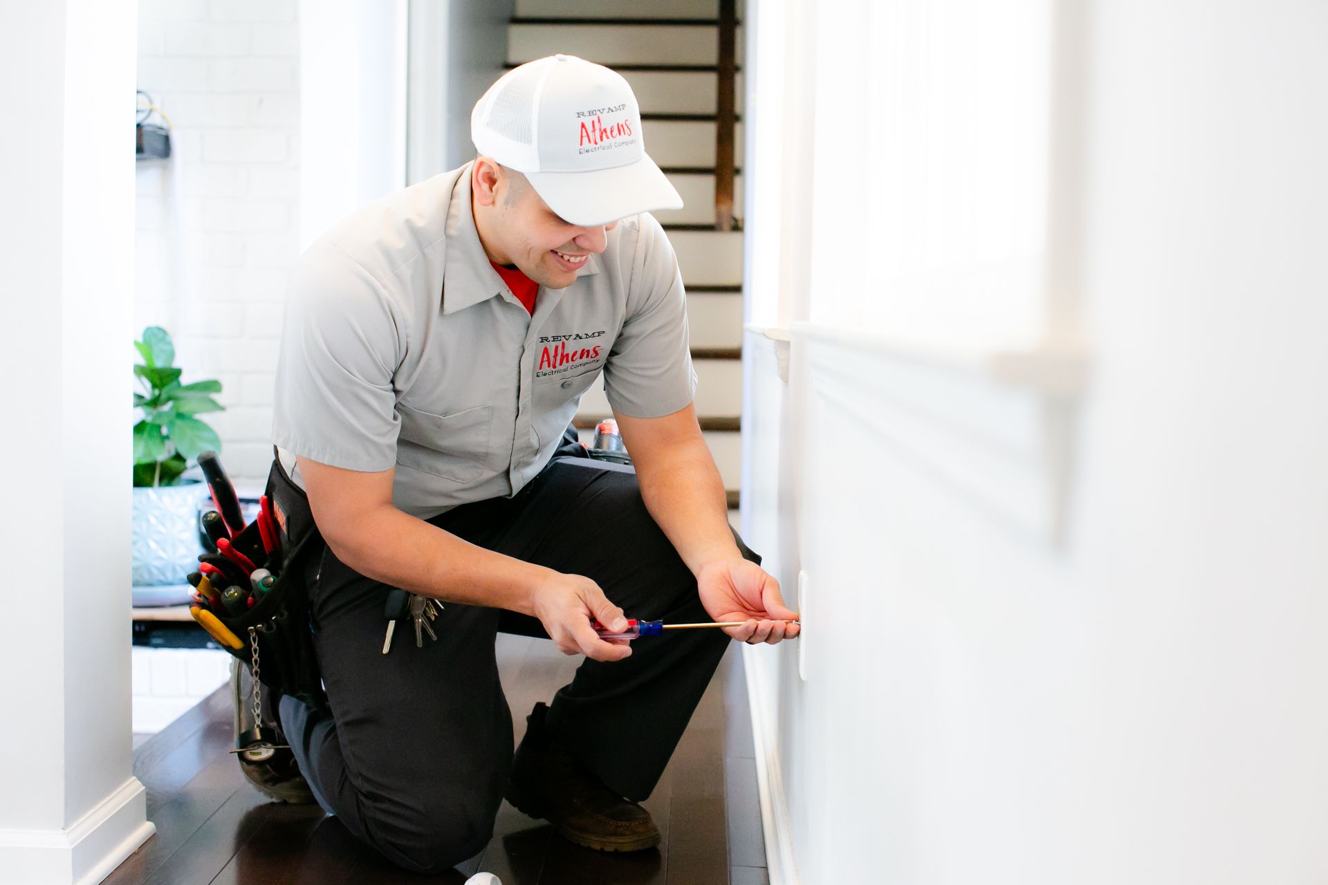 Technician kneeling and inspecting a device near a wall with a tape measure and tools nearby