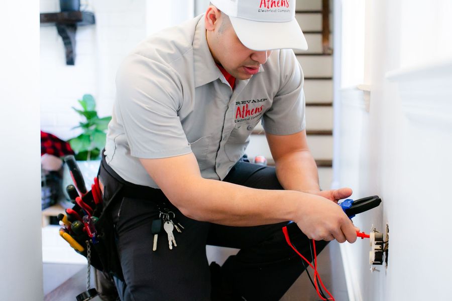 Technician in gray uniform inspecting wiring inside a utility cabinet with tools at his belt.