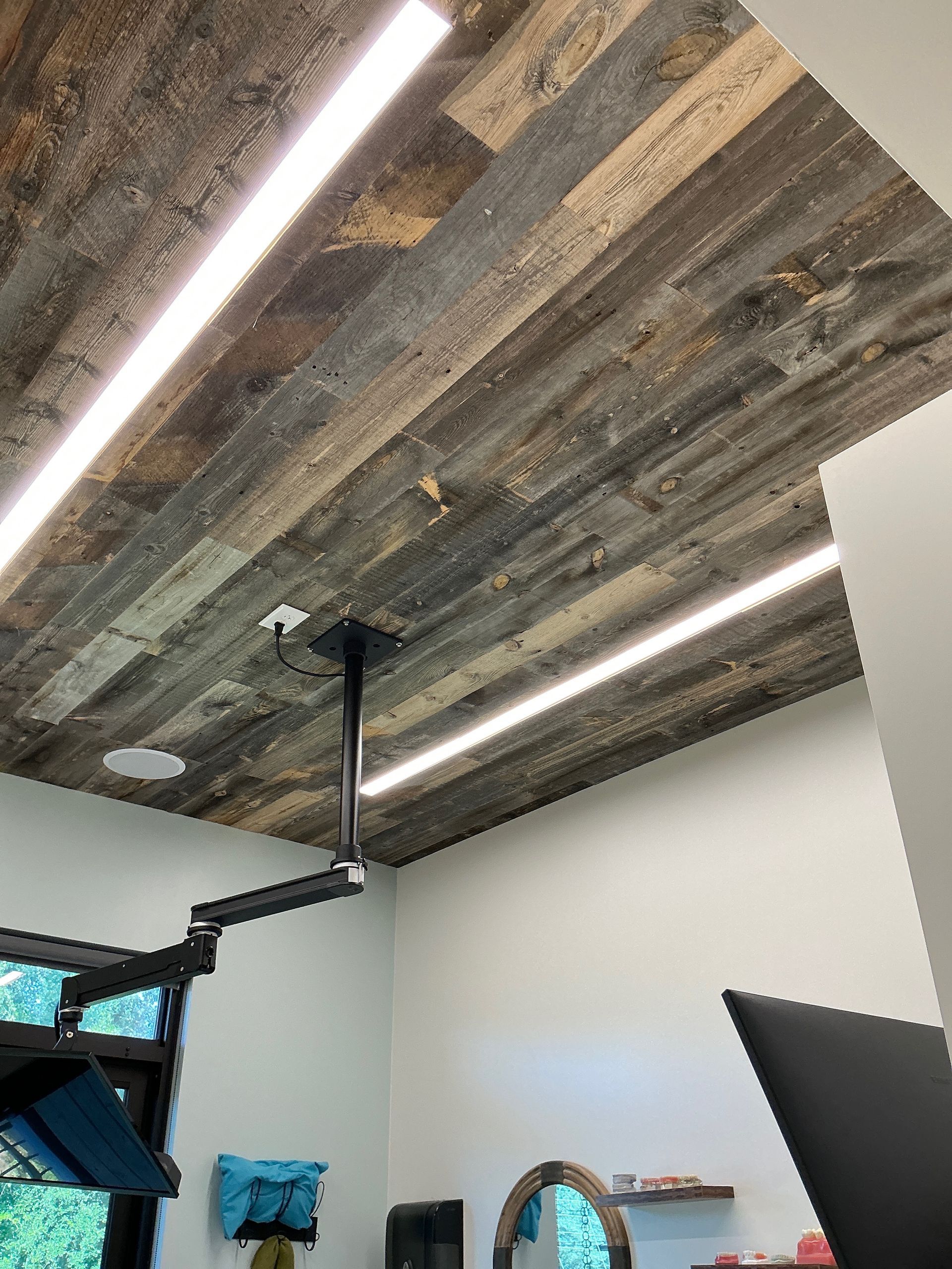 Room with rustic wooden ceiling, ceiling light strips, and a visible projector mount above a home gym area