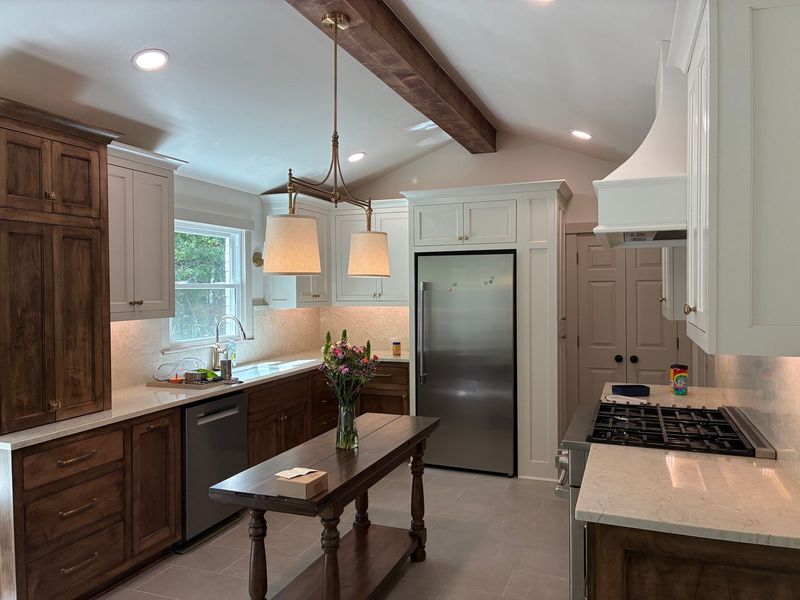 Modern kitchen with dark wood cabinets, stainless fridge, white countertops, and a central island under pendant lights