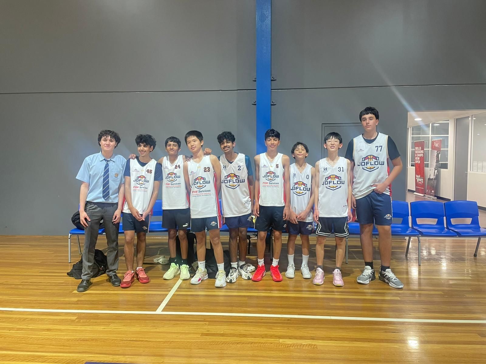 Basketball team poses on court. Players in white jerseys and navy shorts with a coach, indoors.