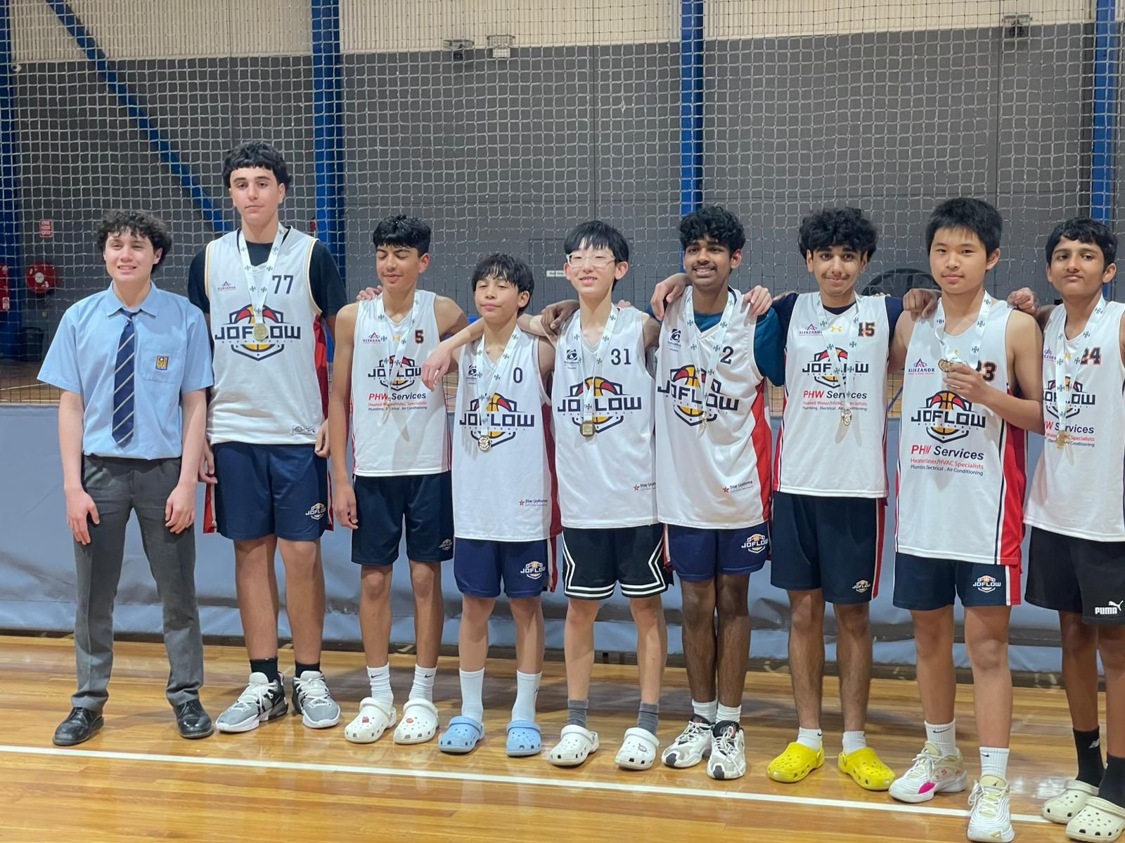 Basketball team in white jerseys poses on a court with a boy in a school uniform.