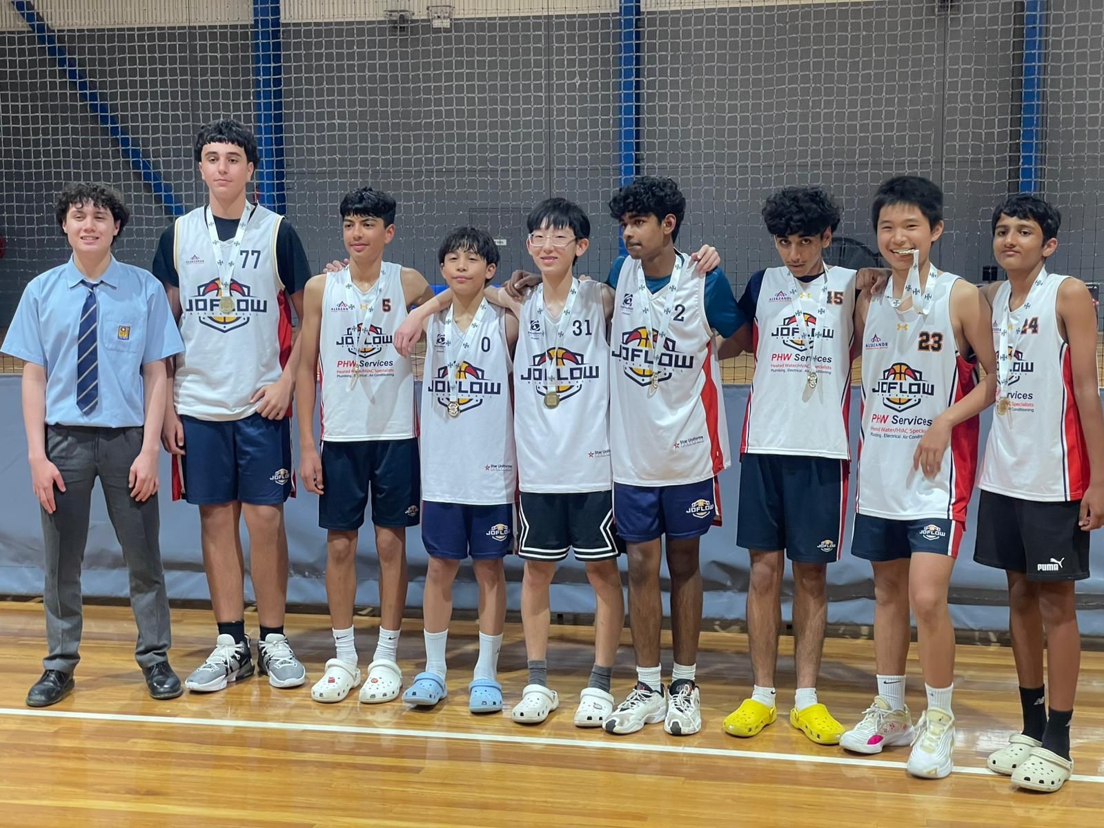 Basketball team poses for a photo on a court, wearing white and blue jerseys.