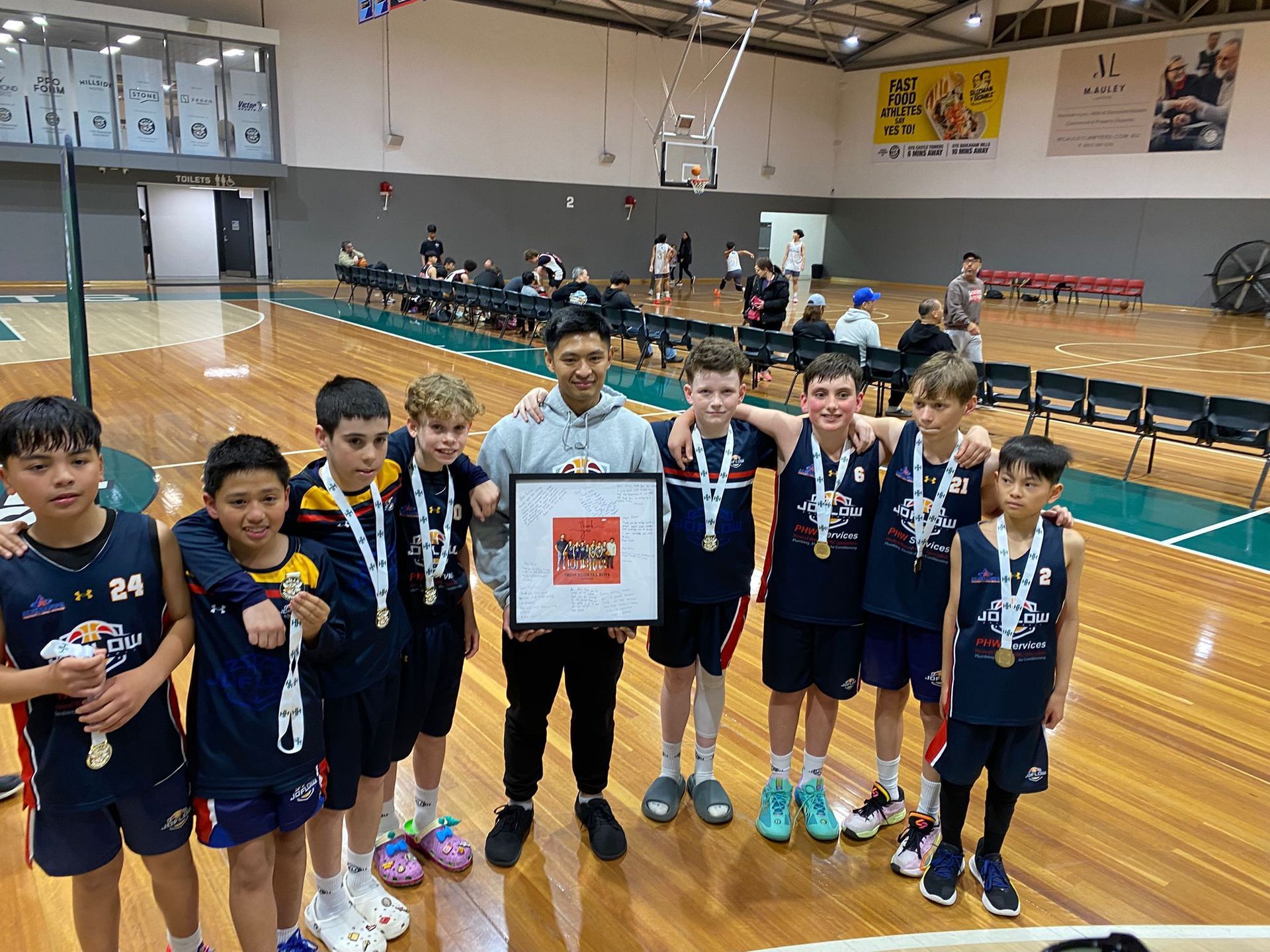 Youth basketball team with medals and a trophy, posing on court.