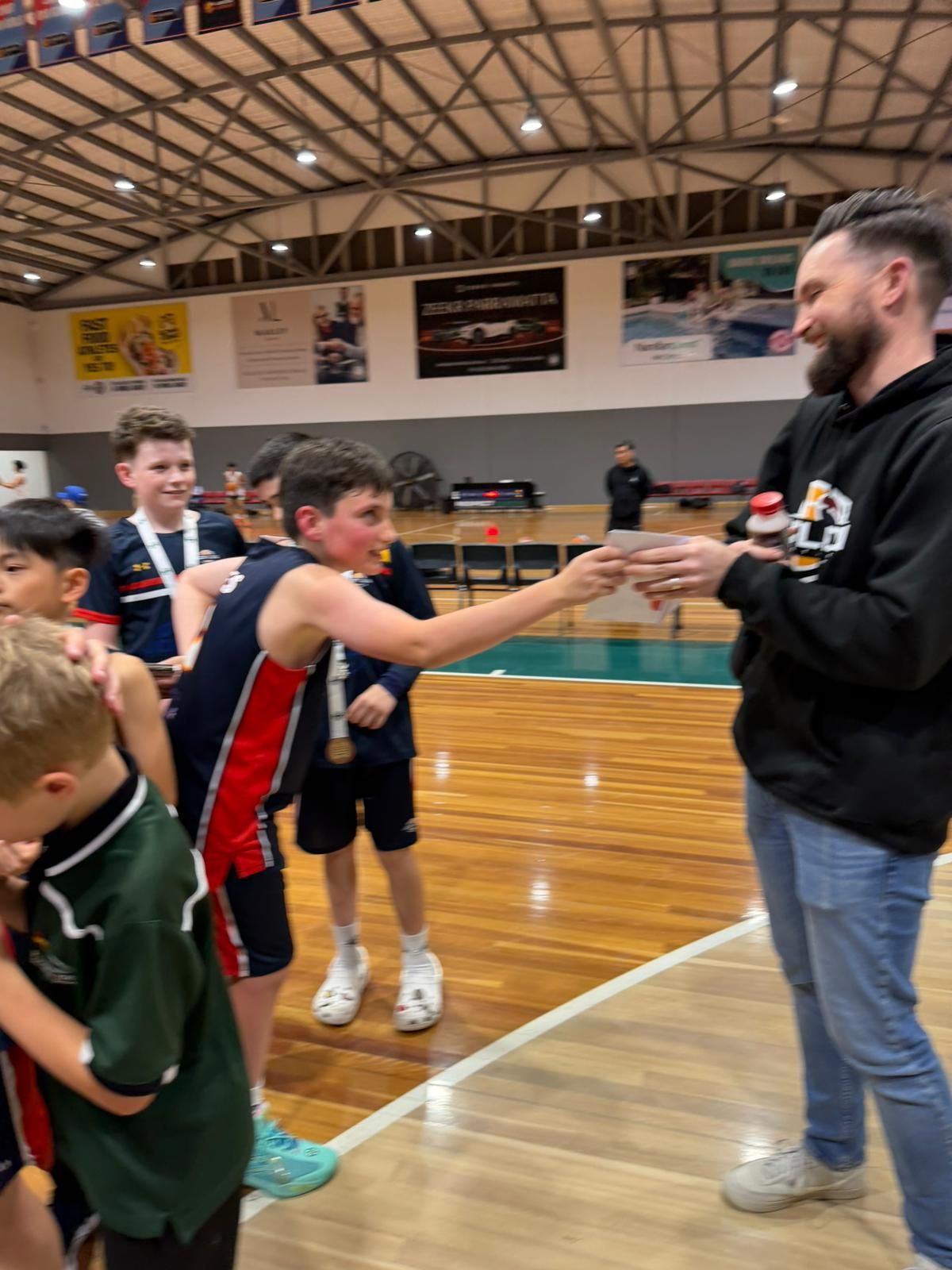 A young boy in a blue and red uniform receiving an award from a man at an indoor basketball court.