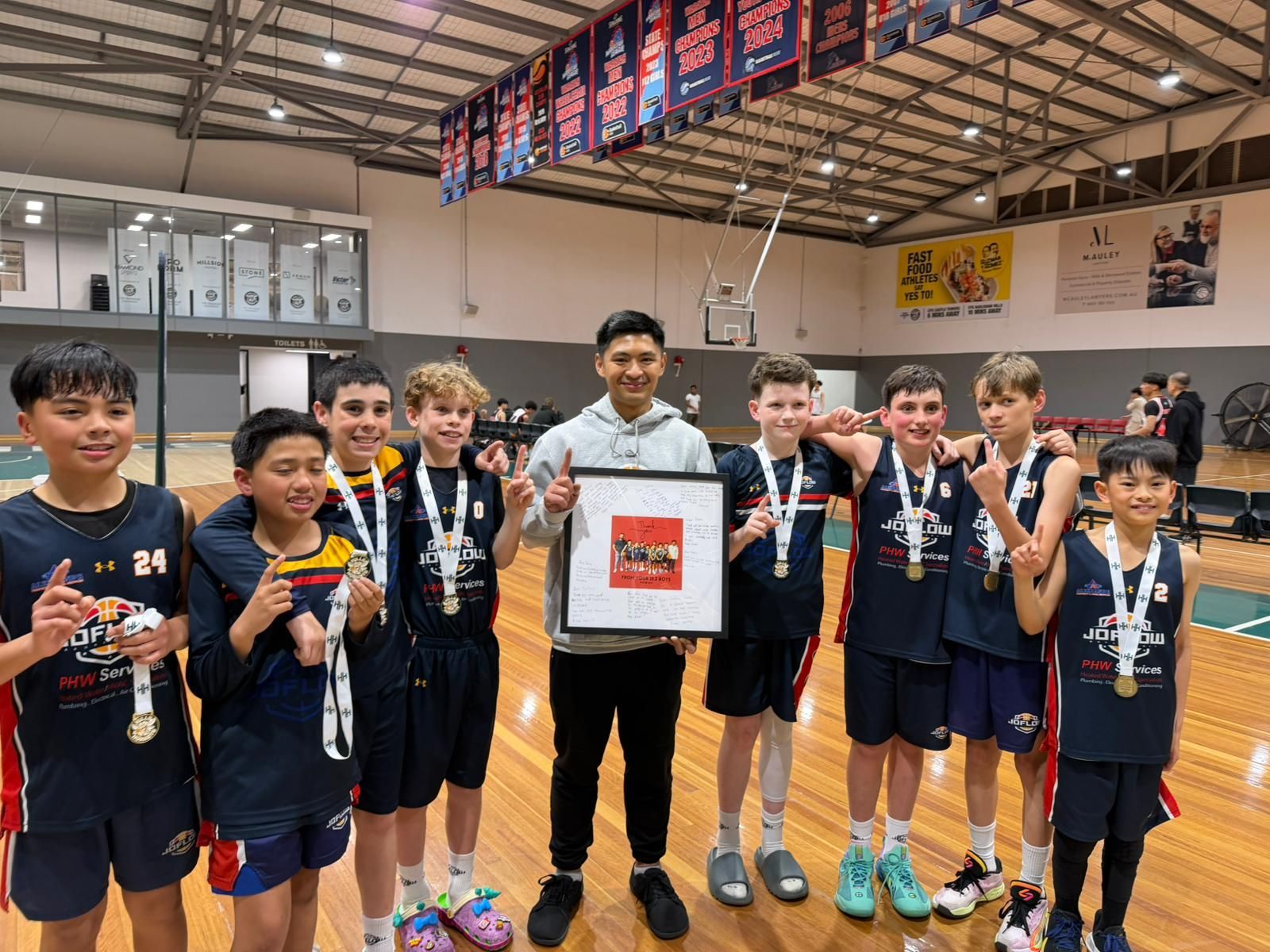 Youth basketball team with medals and trophy posing in a gym.