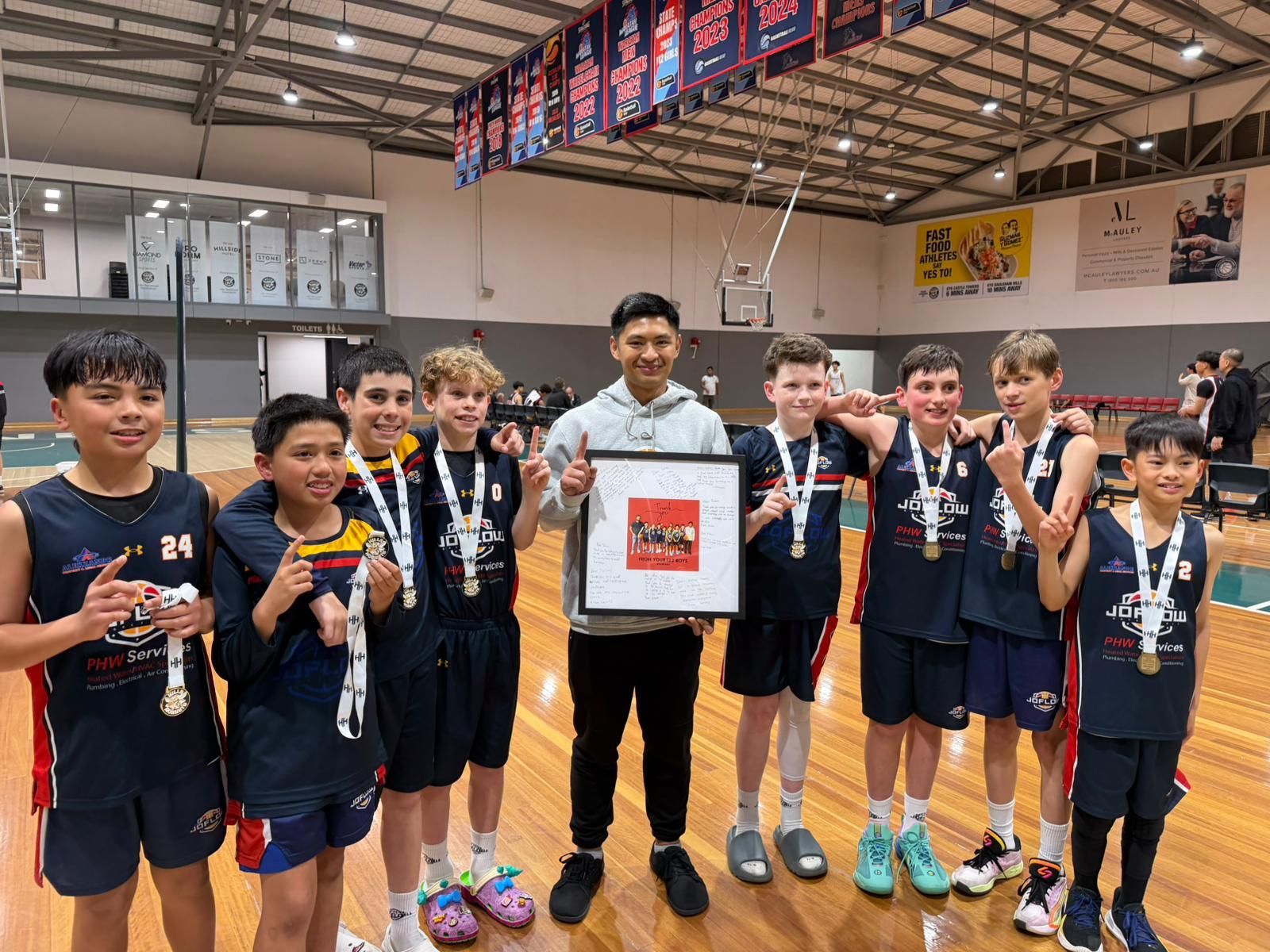 Youth basketball team holding medals and a framed photo in a gymnasium.