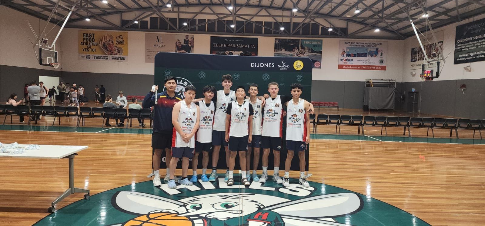 Basketball team posing for a photo in a gymnasium with a green and white court.