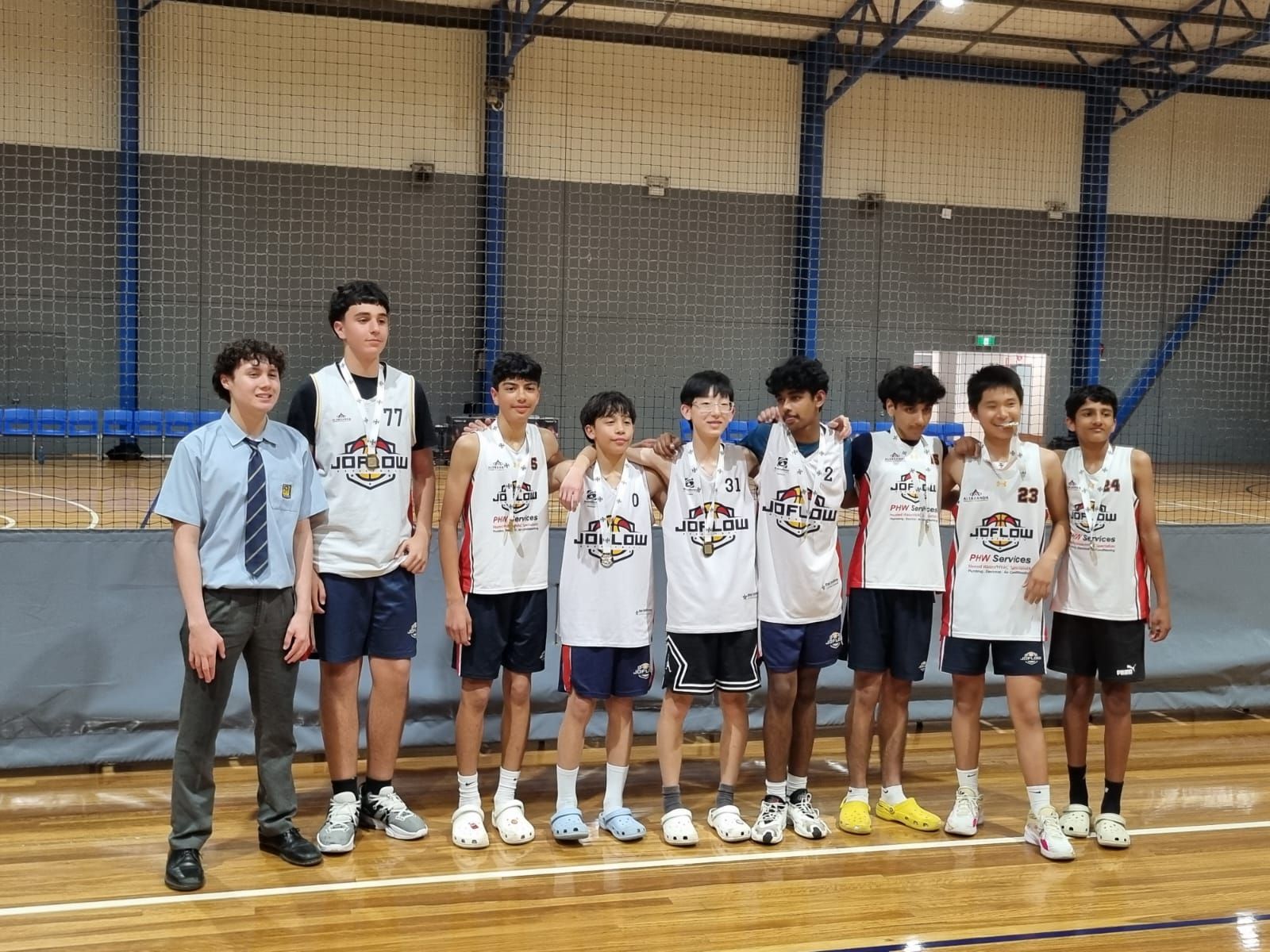 A youth basketball team poses on a court. Boys in jerseys stand with a school staffer.