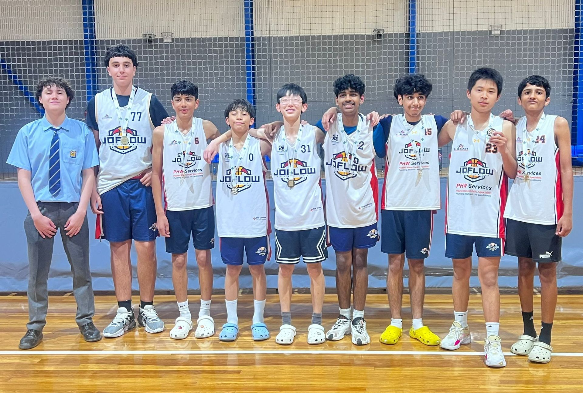 A youth basketball team stands posing. White jerseys, blue shorts, indoor court. Group photo, smiles.