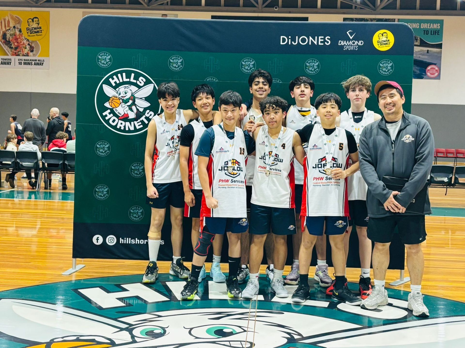 Basketball team, Hills Hornets, poses on court, green backdrop, smiles, black and white uniforms, coach.
