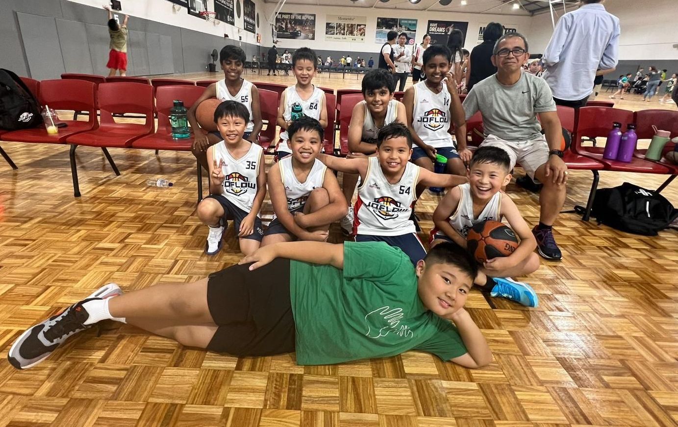 A group of young boys are sitting on a wooden floor with basketballs.