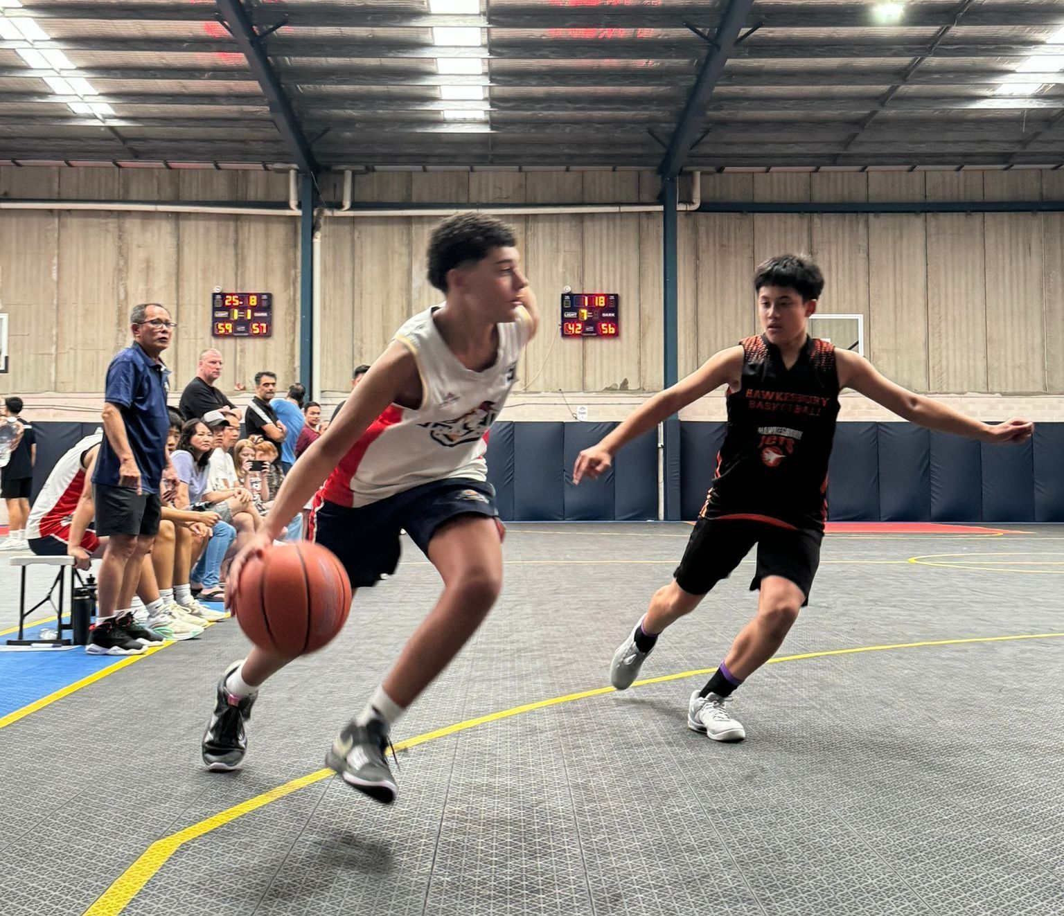 Two young men are playing basketball in a gym.