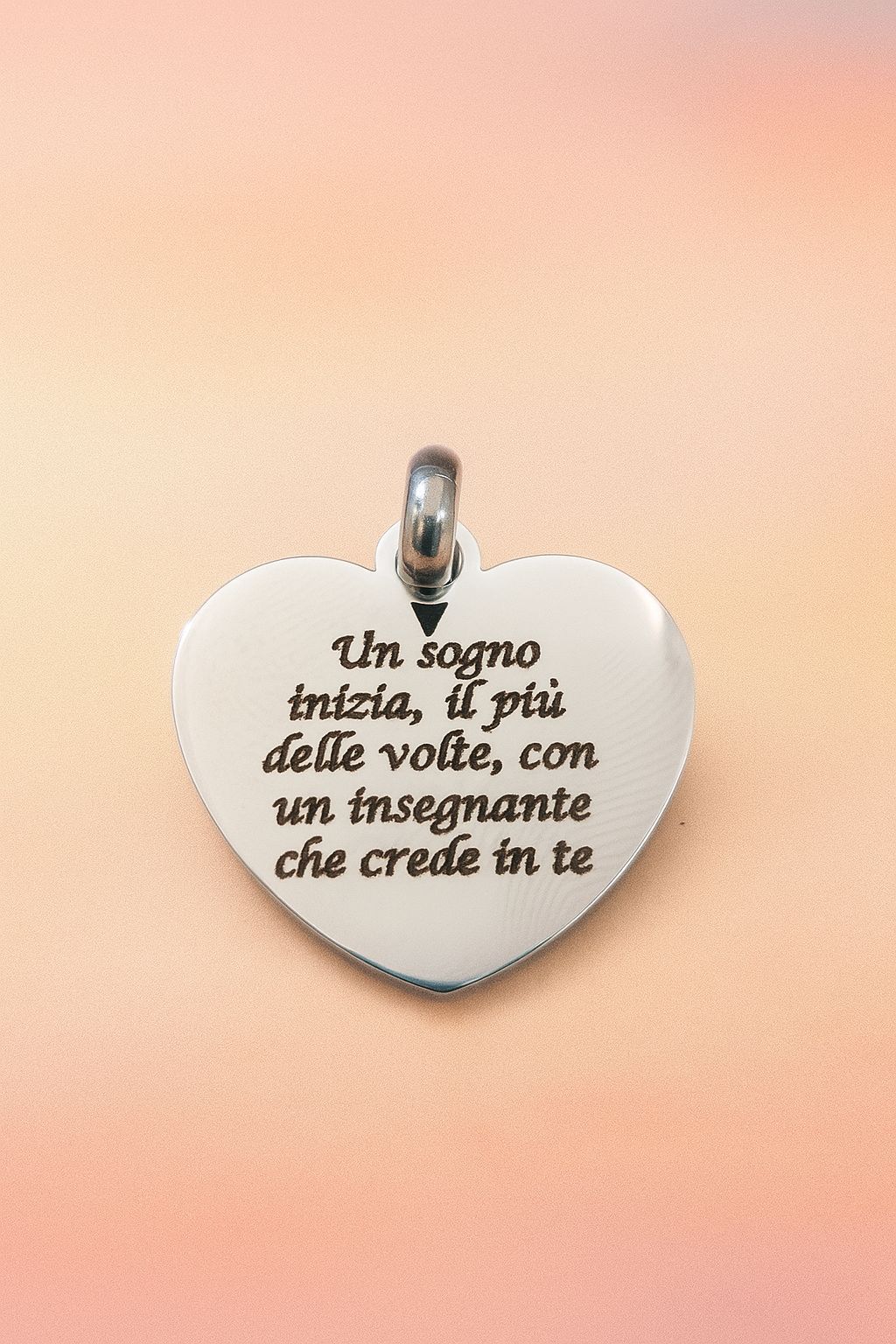 Ciondolo a forma di cuore con testo in italiano, probabilmente un regalo per un insegnante, su uno sfondo rosa.