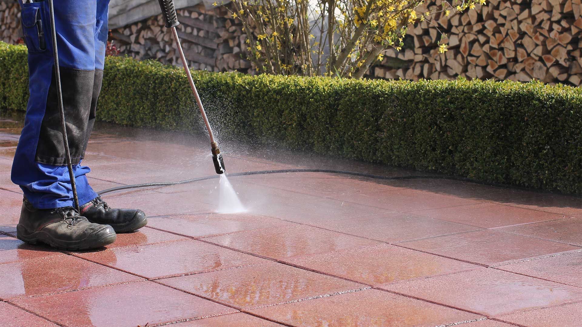 A man is using a high pressure washer to clean a patio.