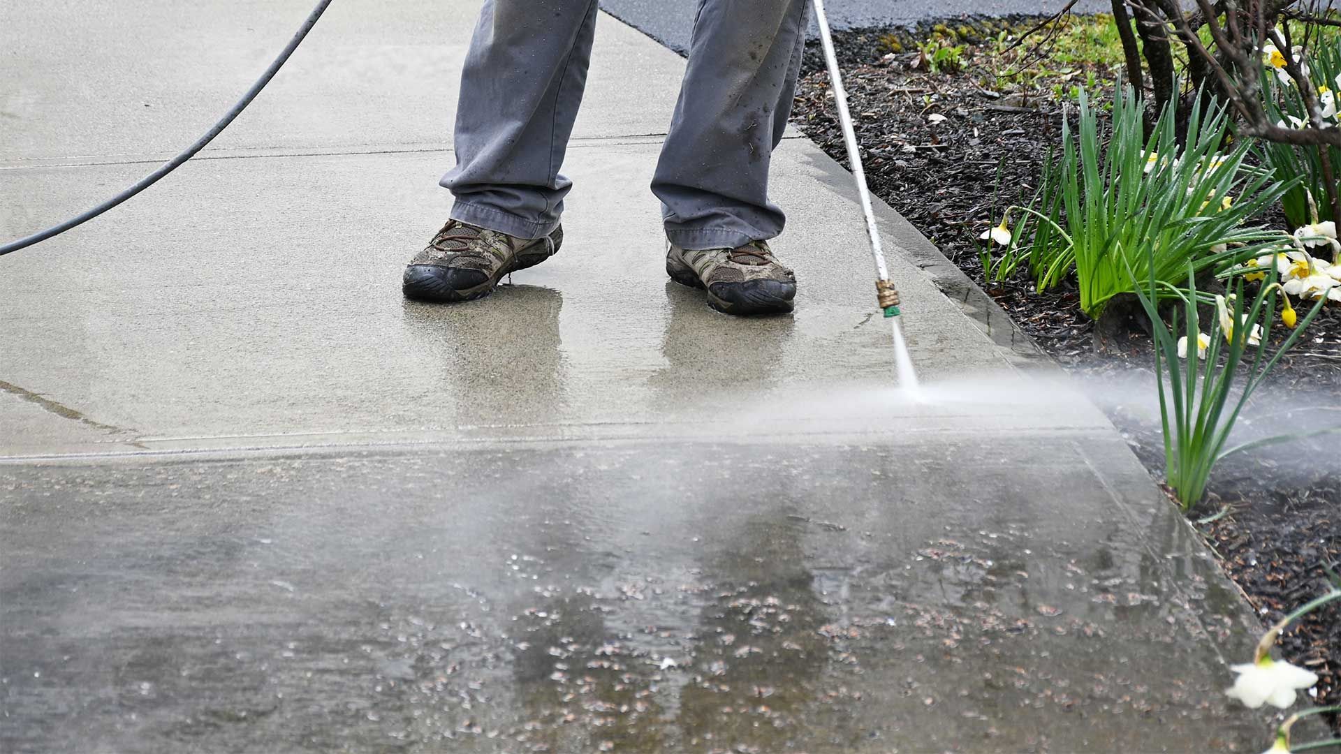 A person is using a high pressure washer to clean a sidewalk.