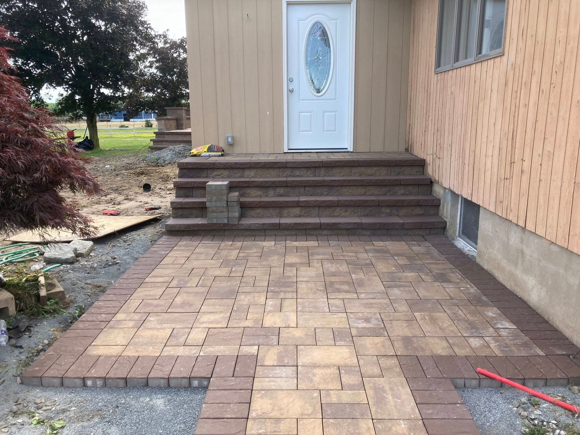Brick paved patio and steps leading to a white door. Brown and tan bricks. Building has tan siding.