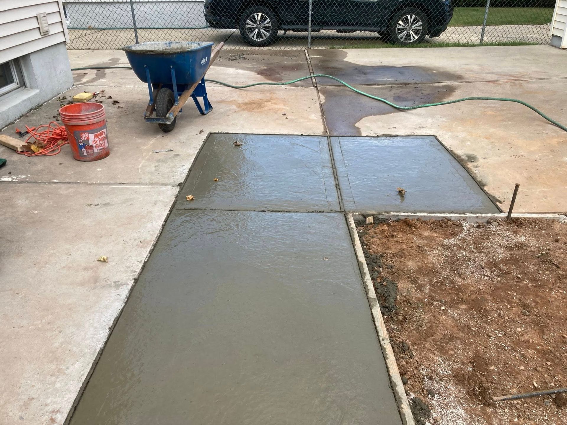 Freshly poured concrete sidewalk sections next to a dirt area, with a wheelbarrow and bucket nearby.