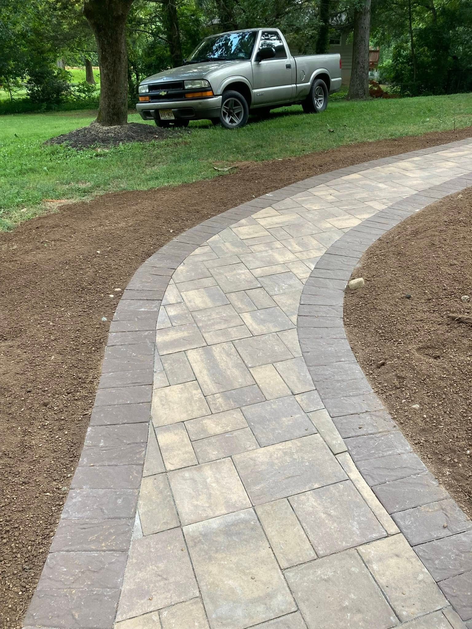 Brick pathway curving through yard; silver pickup truck parked nearby.