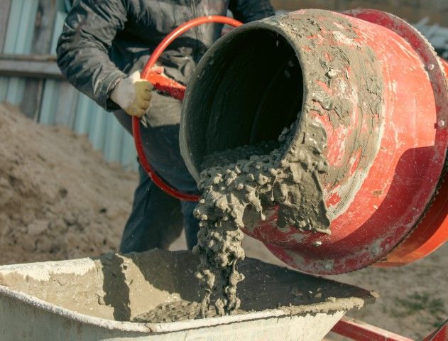 Cement mix pouring from a red concrete mixer into a wheelbarrow outdoors