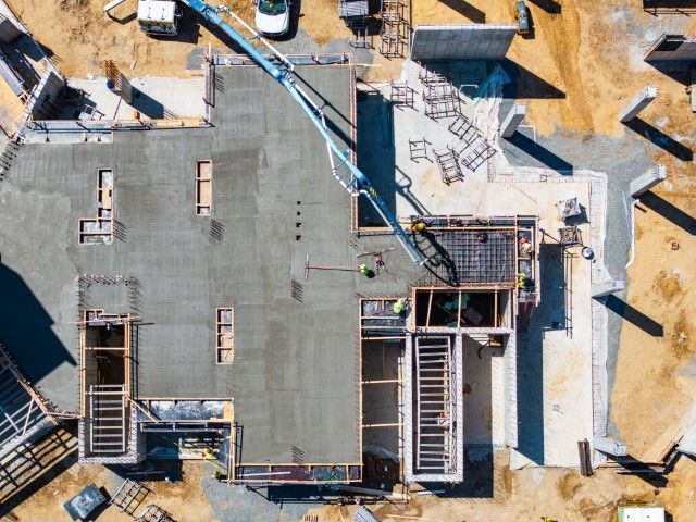 Aerial view of a flat-roof building under construction with scaffolding and surrounding dirt site