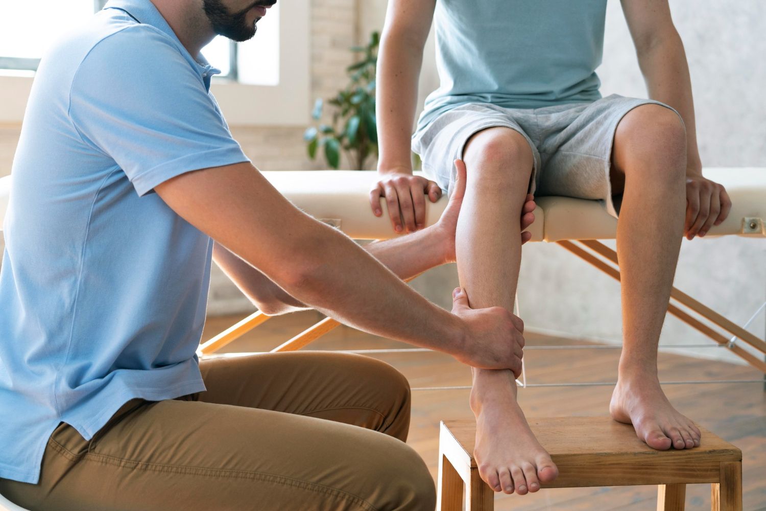 A man and a woman are sitting on the floor in a gym . the woman is bandaging the man 's ankle.