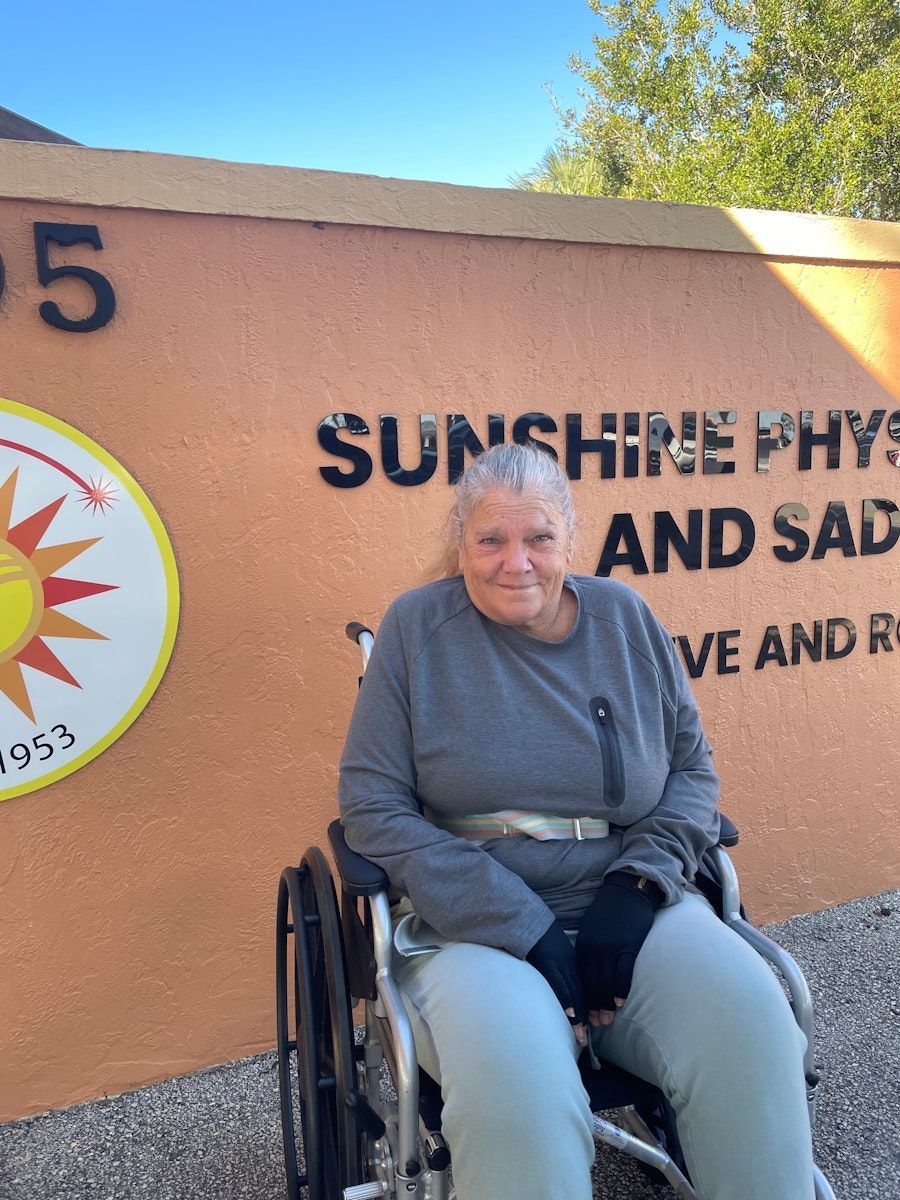 A woman in a wheelchair is sitting in front of a sign that says sunshine and sad.