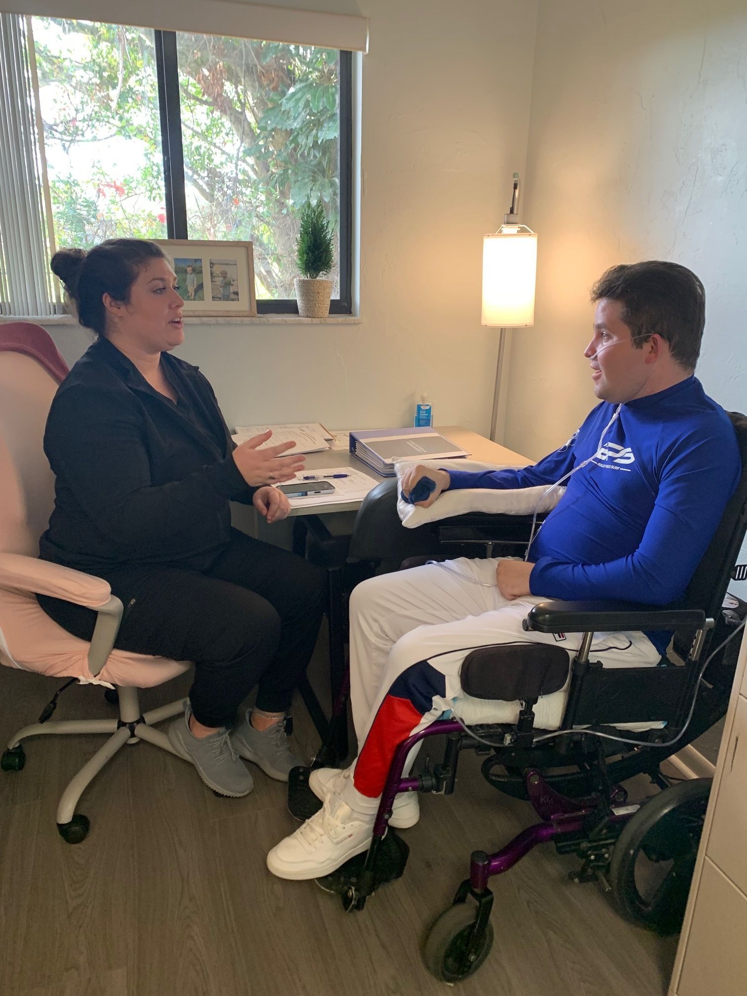 A man and a woman are sitting on the floor in a gym . the woman is bandaging the man 's ankle.