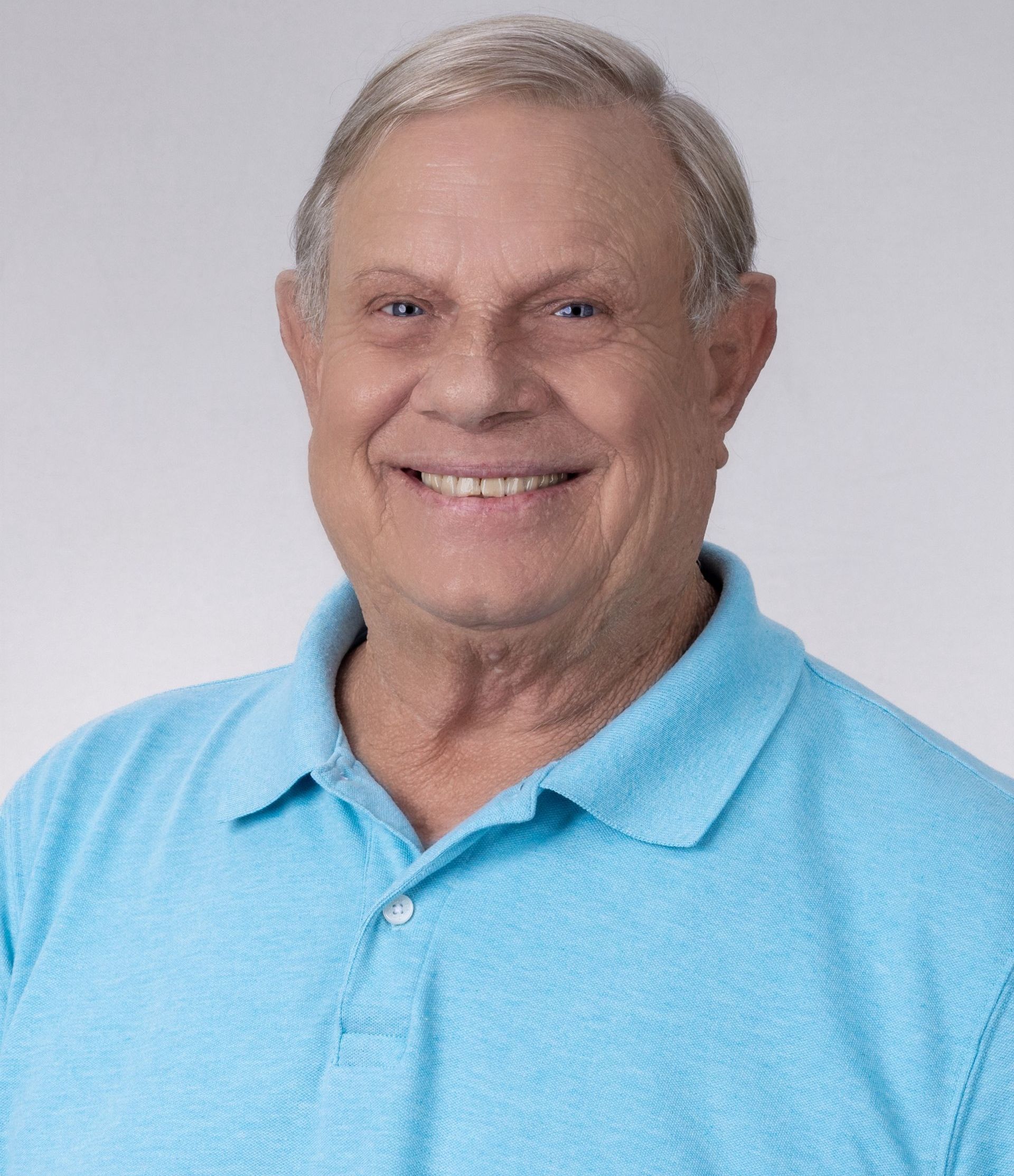 A man wearing glasses and a blue shirt is smiling for the camera.