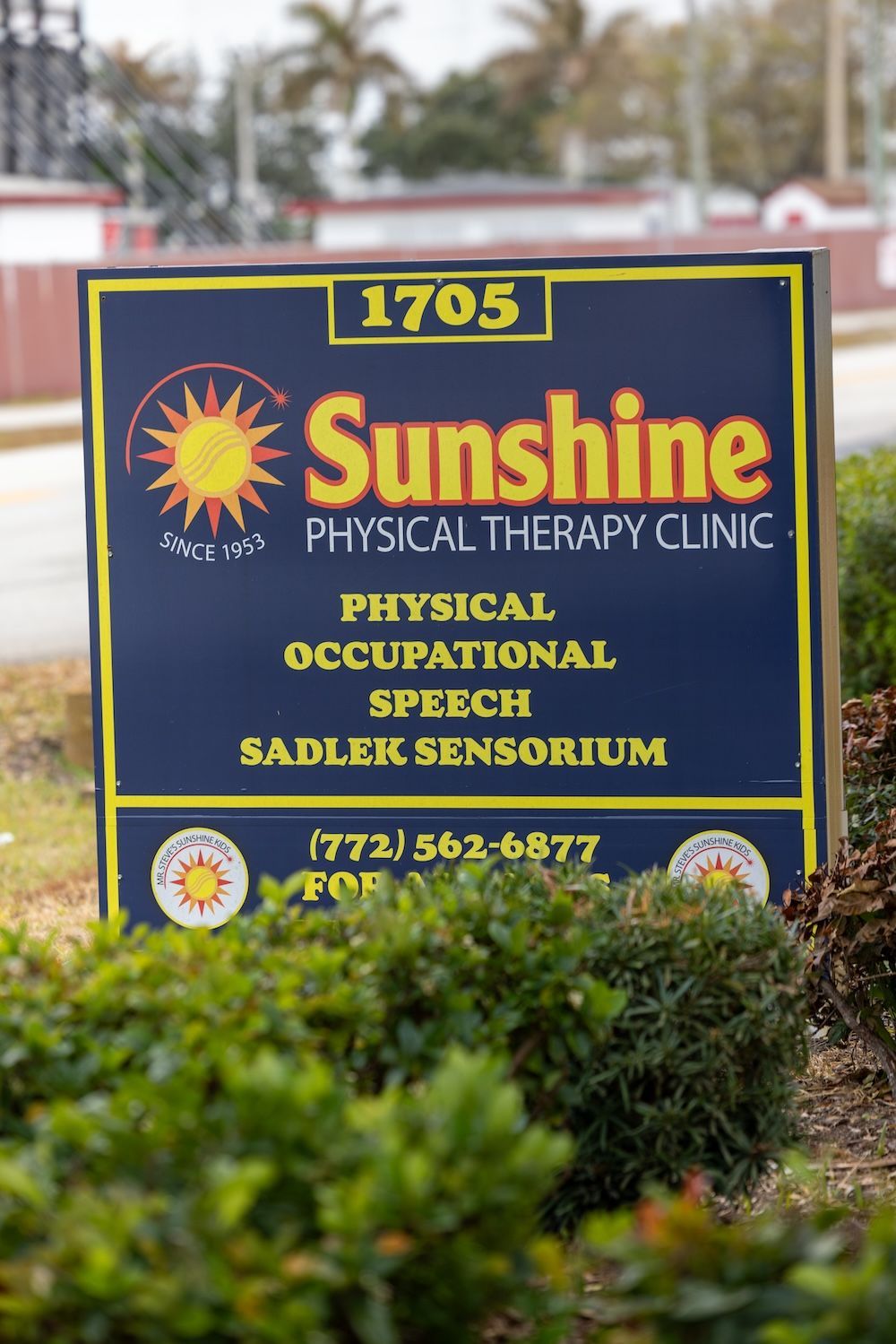 A woman wearing glasses and earrings is standing in front of a painting.