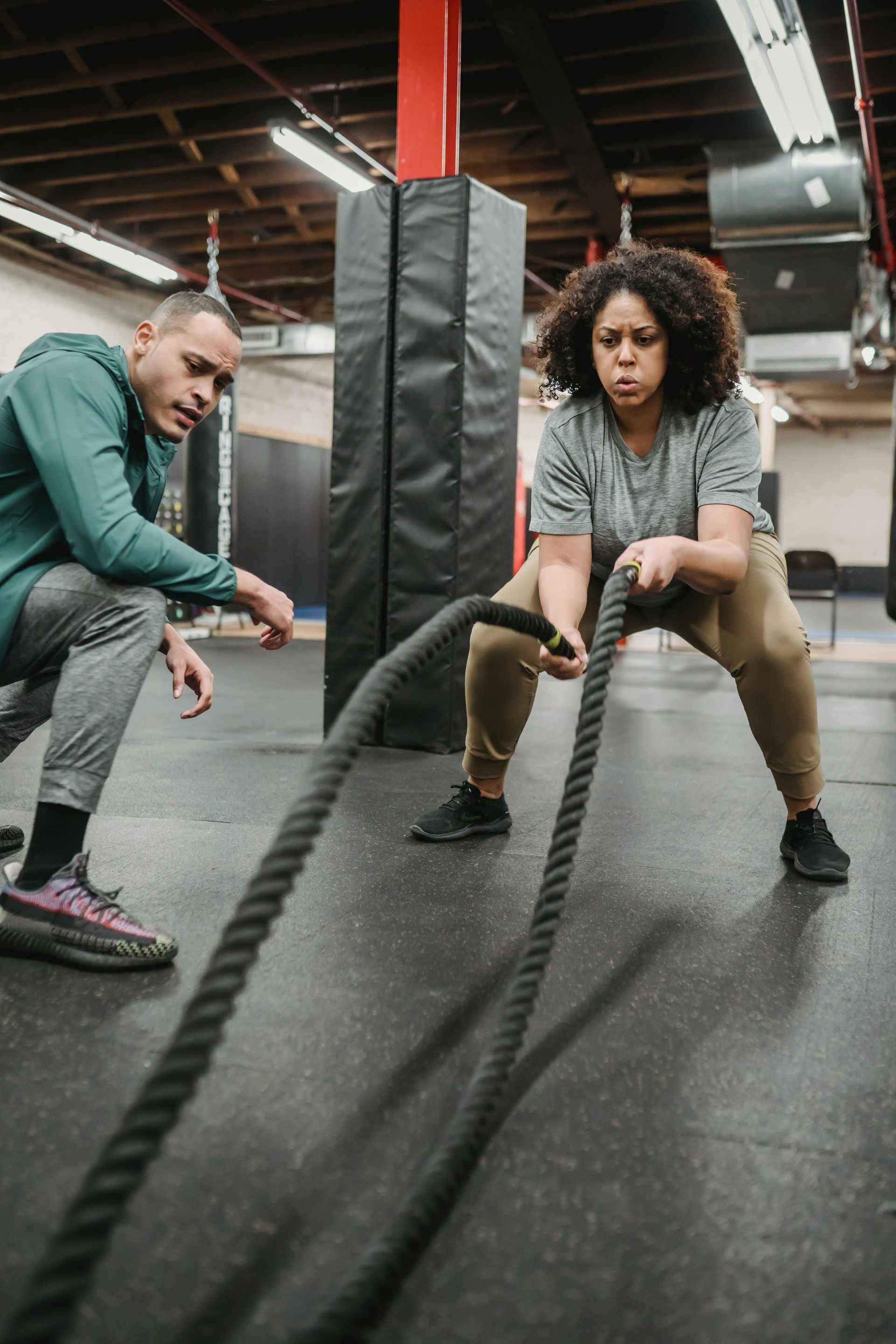 A man and a woman are sitting on the floor in a gym . the woman is bandaging the man 's ankle.