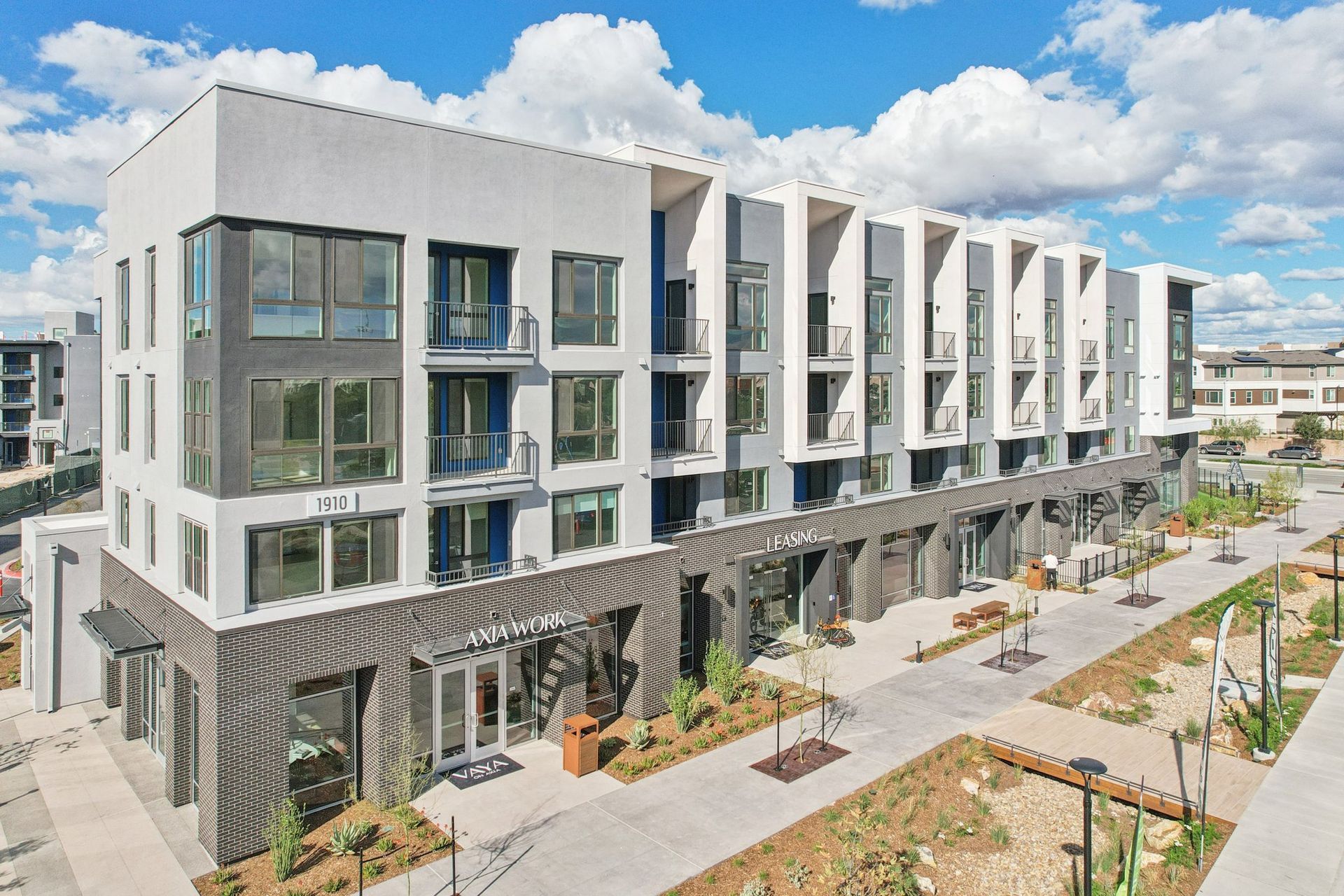 Modern multi-story building with storefronts and outdoor walkway on a sunny day.