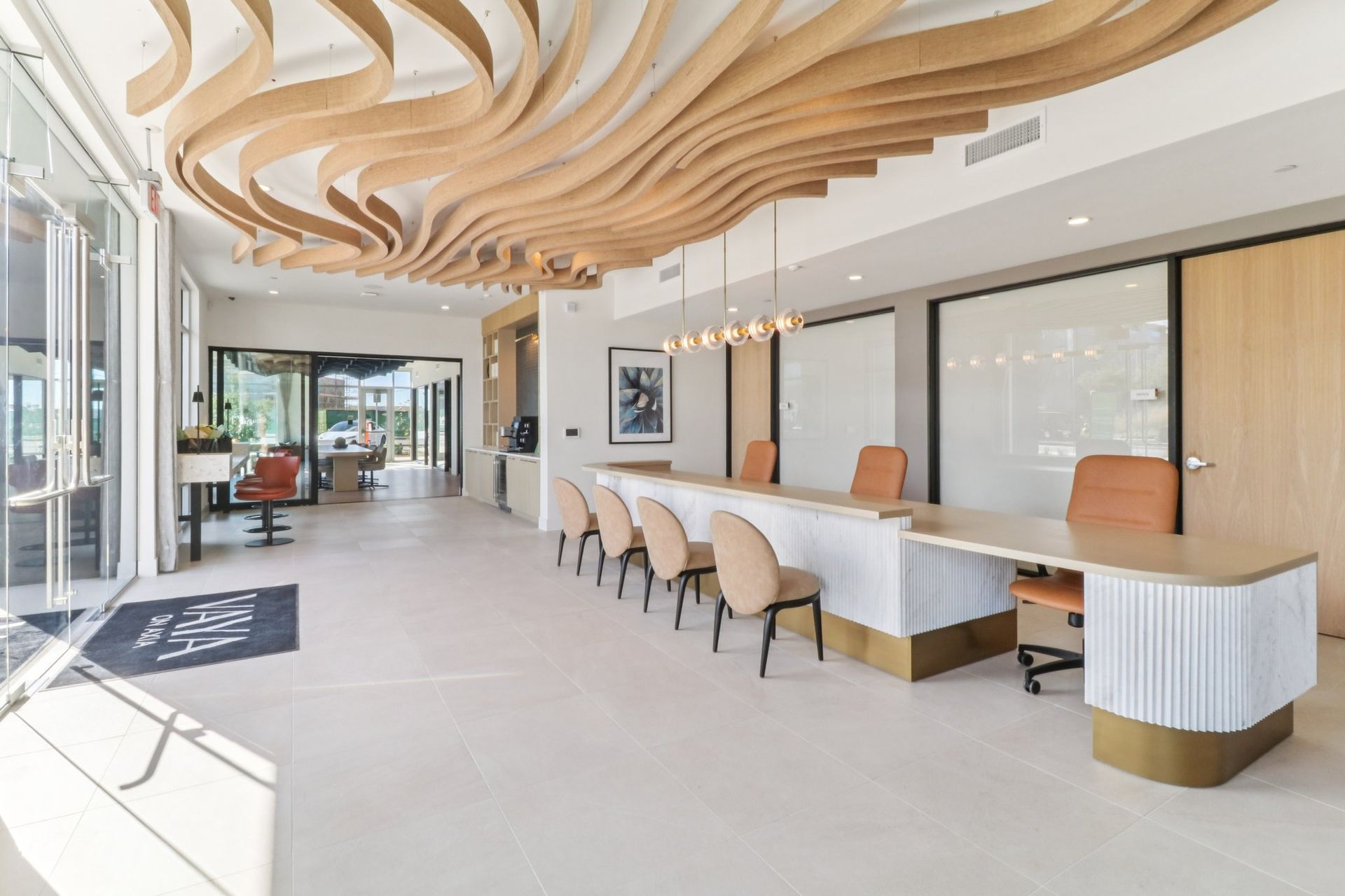 Reception area with wooden wave-like ceiling, long counter, chairs, and glass doors.