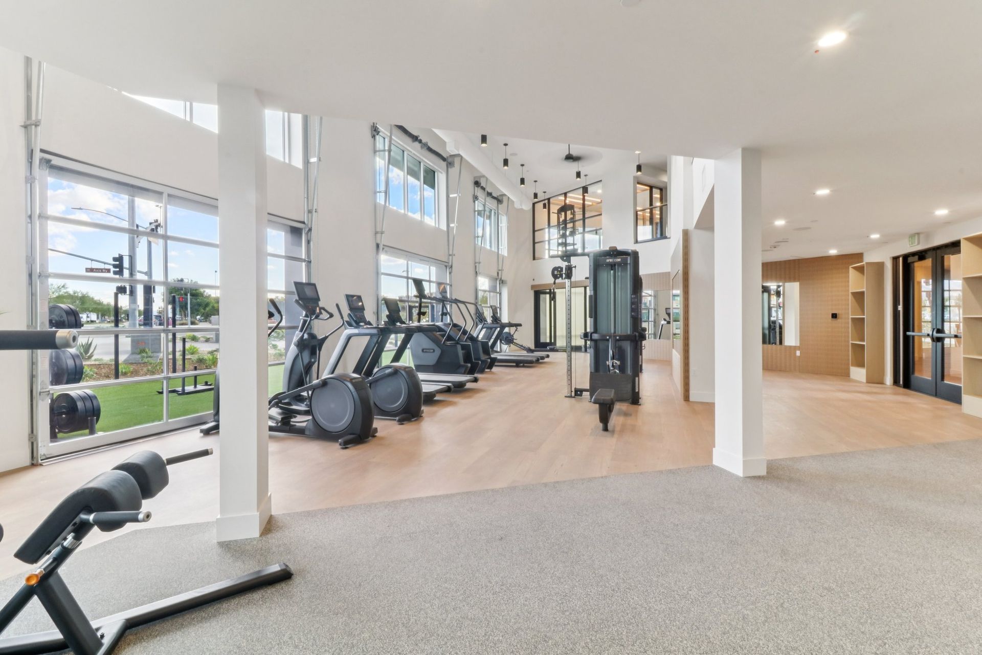 Gym interior with cardio machines, weight bench, and large windows.