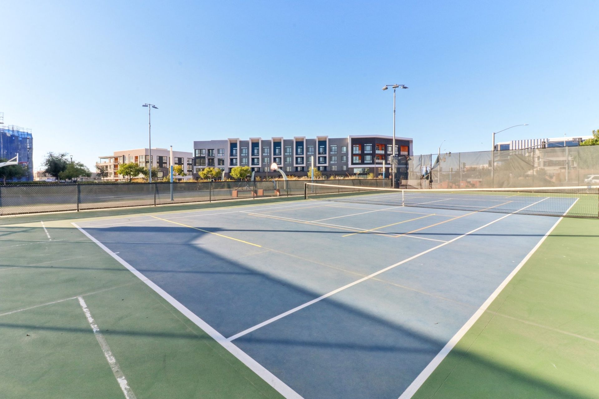 Tennis court with blue and green surface; modern apartment building in the background.