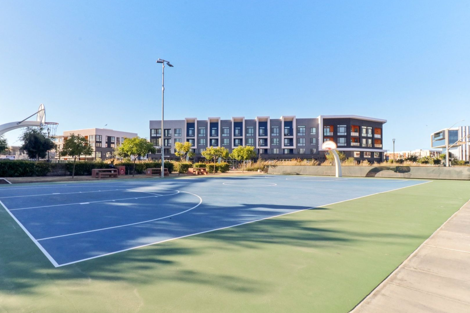 Outdoor basketball court with a modern building in the background on a sunny day.