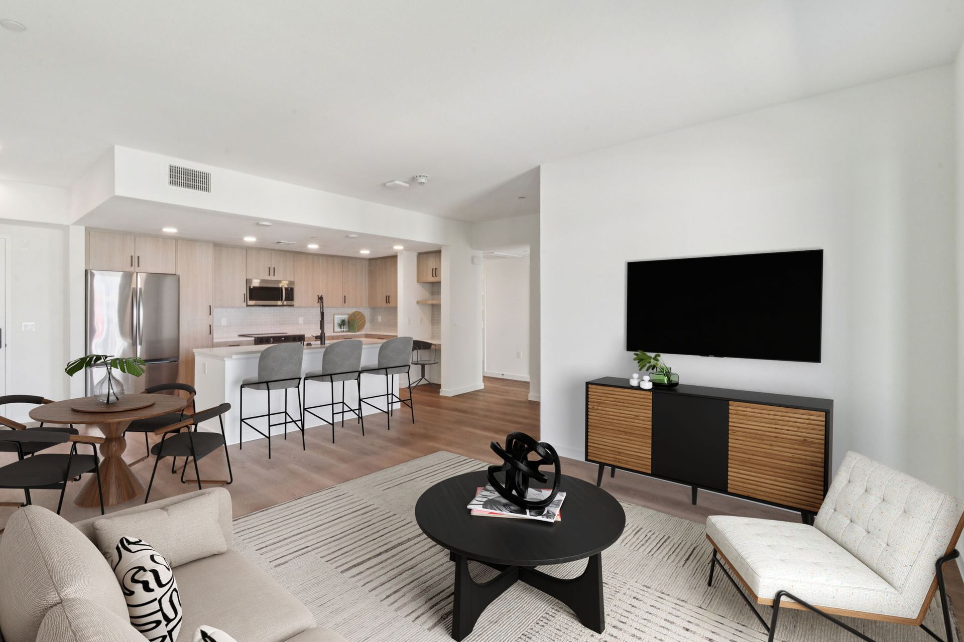 Modern living room with open kitchen, light wood floors, and neutral furnishings.