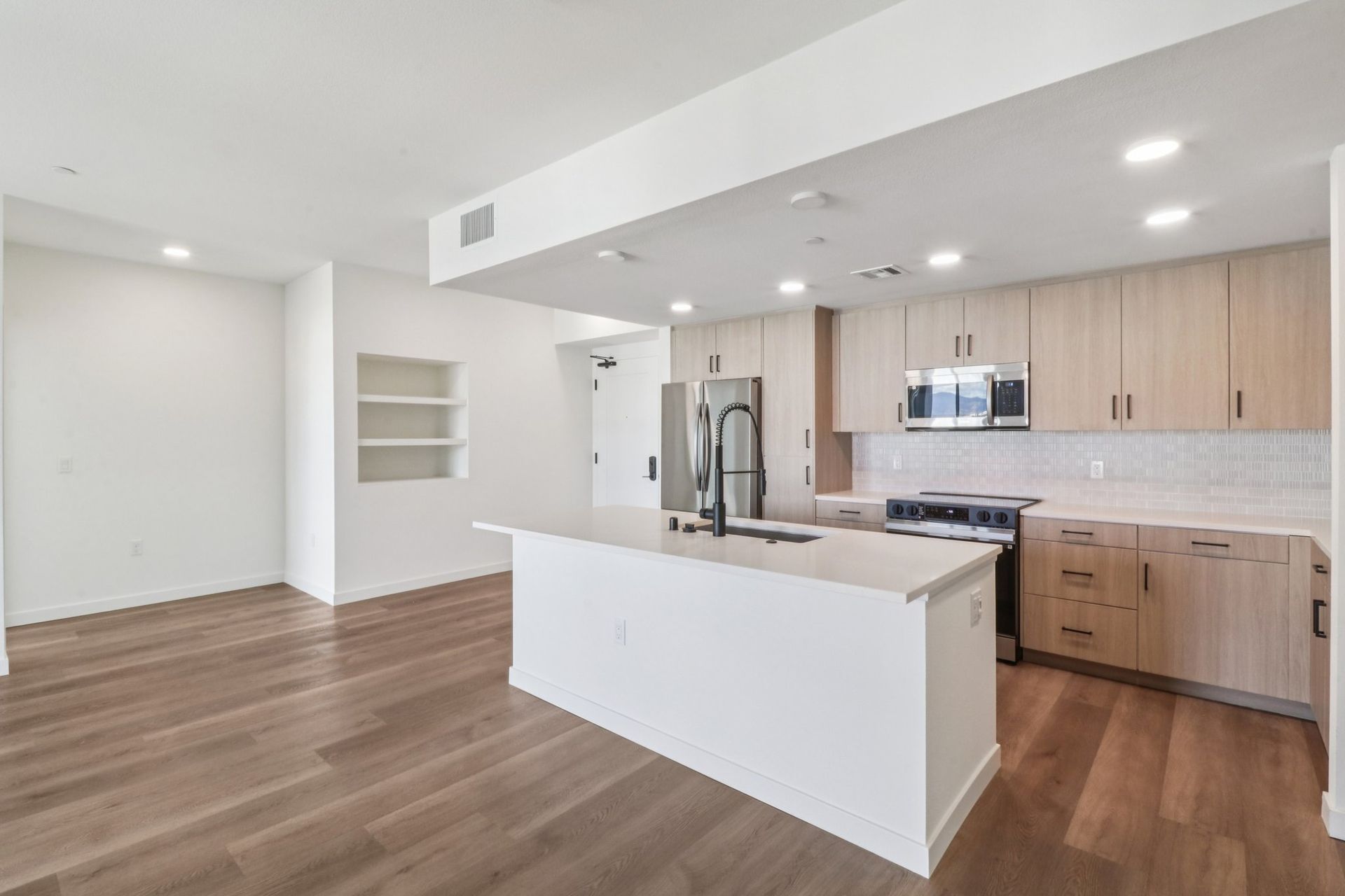 Modern kitchen with light wood cabinets, white island, stainless steel appliances, and hardwood floors.