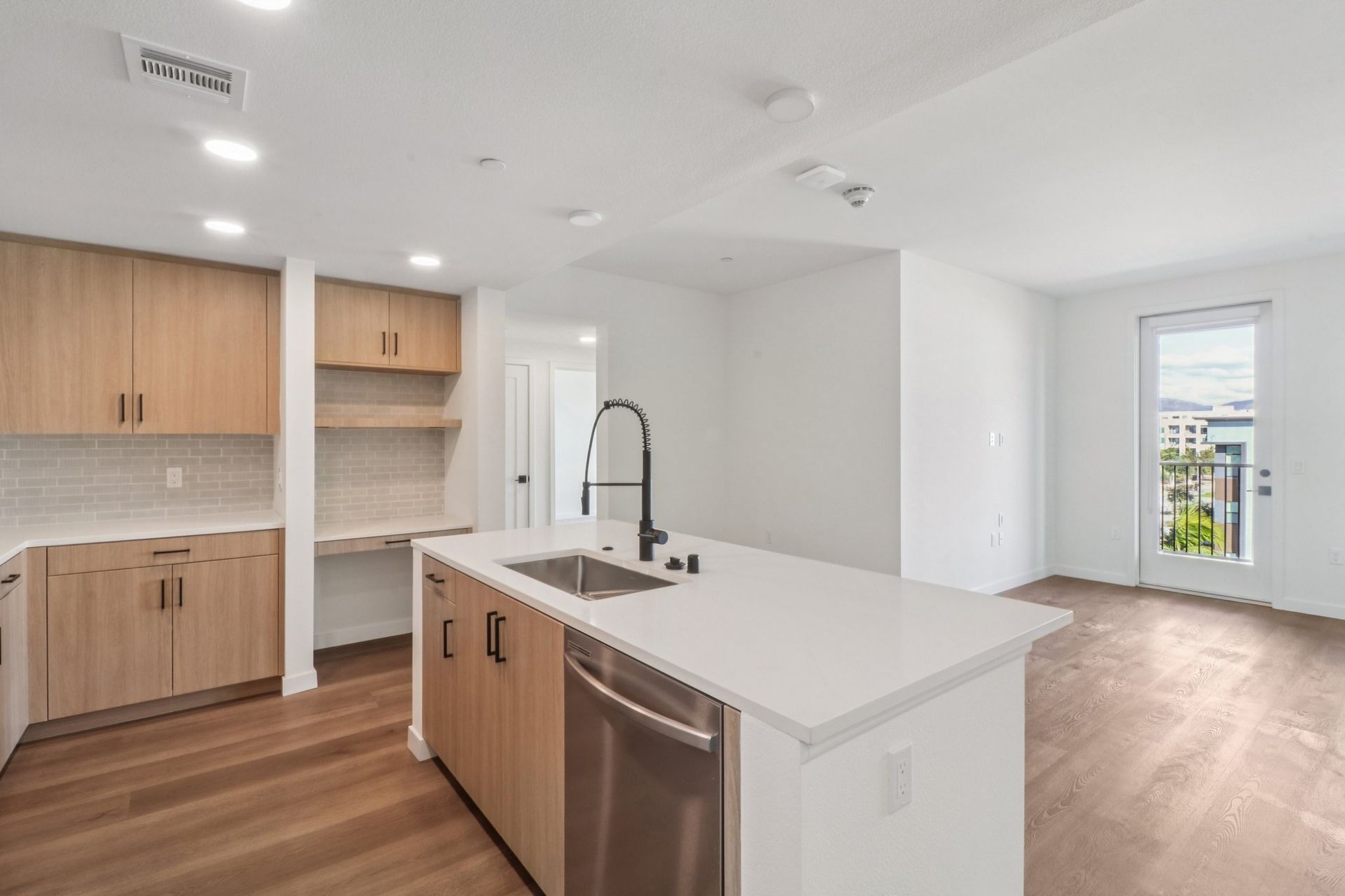 Modern kitchen with light wood cabinets, white countertops, and stainless steel appliances.